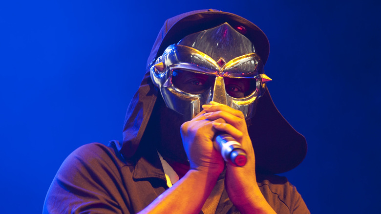 MF Doom on stage with hands on mic in mask and hood