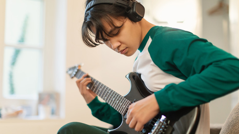 A young man playing guitar through headphones