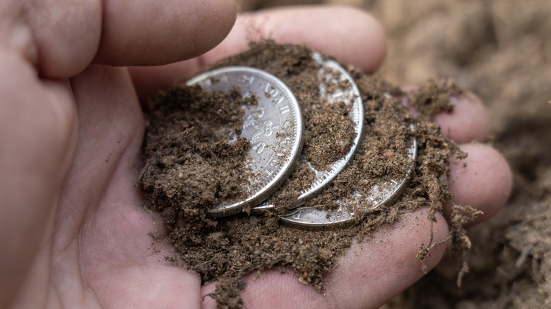 coins in dirt in hand