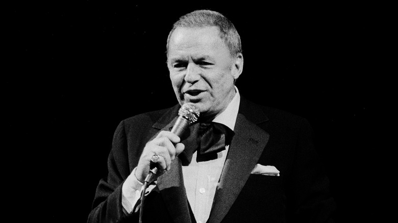 Frank Sinatra singing in suit on stage with black background in '70s