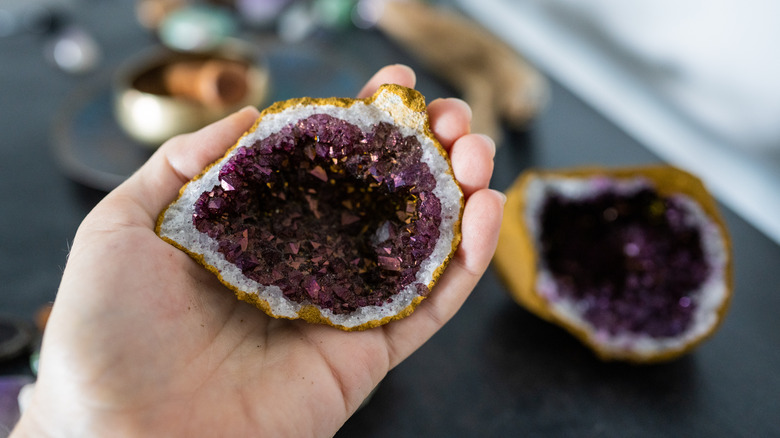 A deeply colored amethyst geode, held in someone's hand