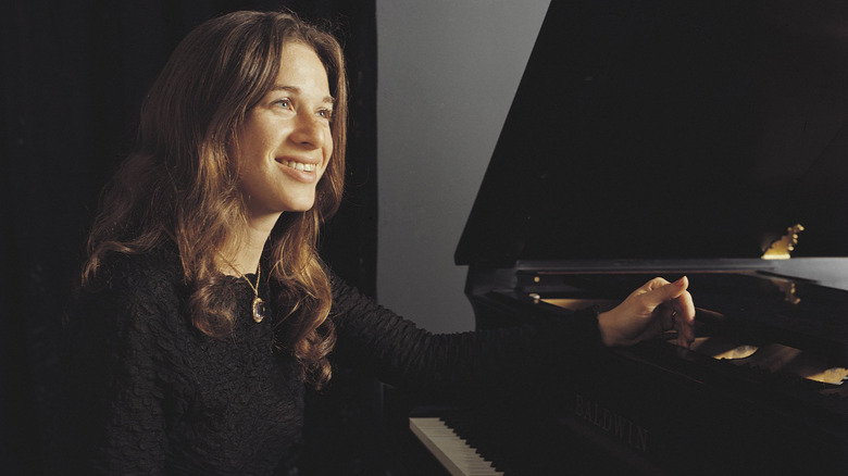 Carole King smiling while sat at a piano