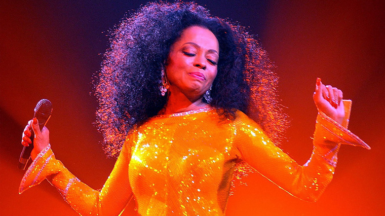 Diana Ross performing onstage wearing a glittery orange outfit