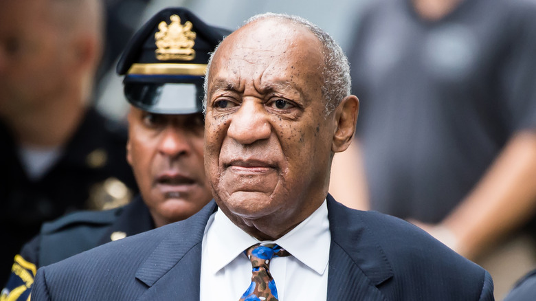 Bill Cosby outside of court, with a police officer standing behind him