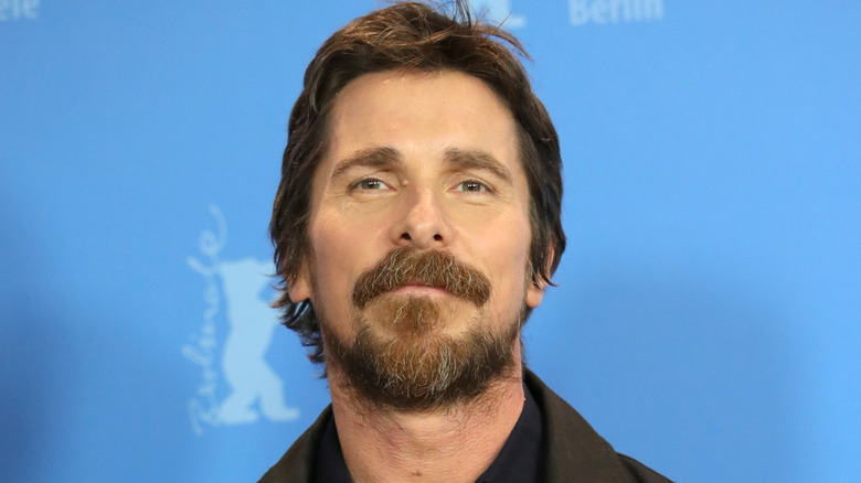 Christian Bale bearded in front of a blue background