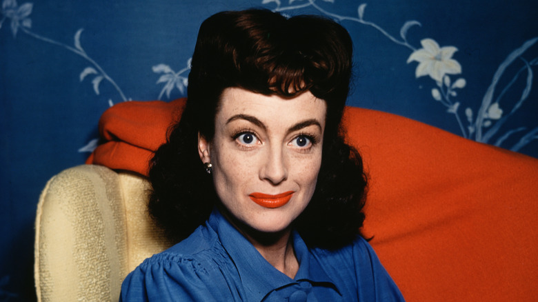 Joan Crawford sitting on a chair in front of blue floral wallpaper