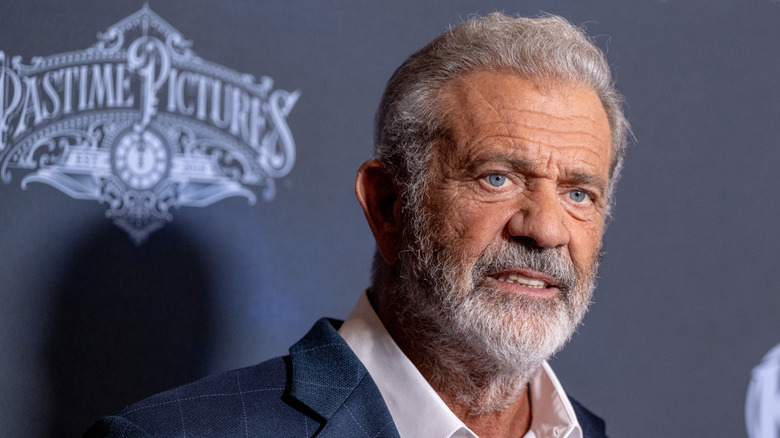 Mel Gibson with a beard, posing in front of a grey-blue background