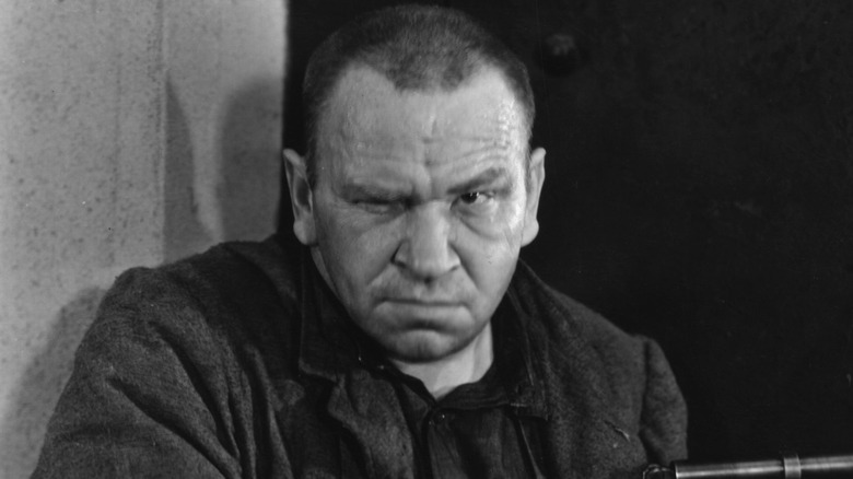 Wallace Beery scowling in dark jacket by wall