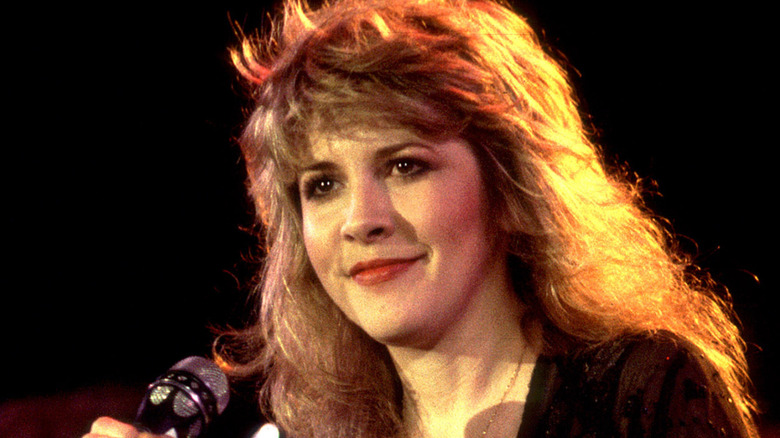 Stevie Nicks smiling onstage while holding microphone in 1983