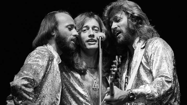 The Bee Gees singing together in shiny suits on stage