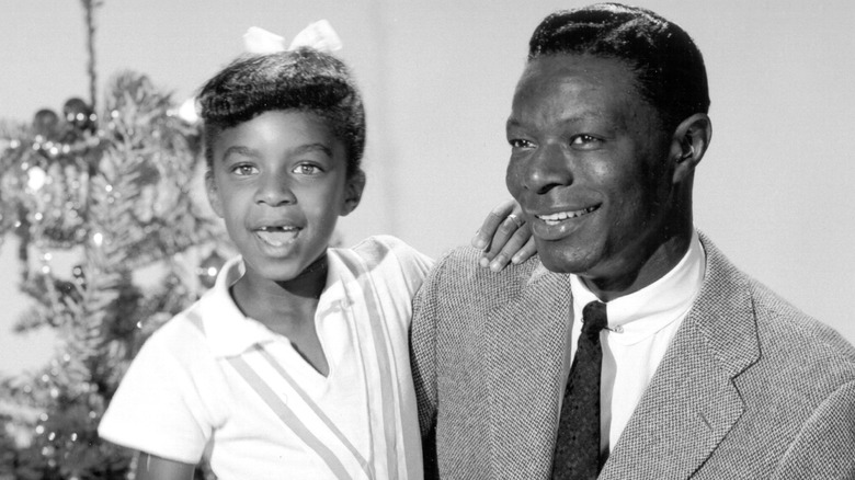 Young Natalie Cole smiling with Nat King Cole by Christmas tree
