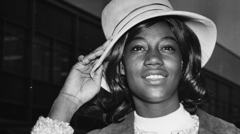 Kim Weston smiling and adjusting hat at London airport in 1964