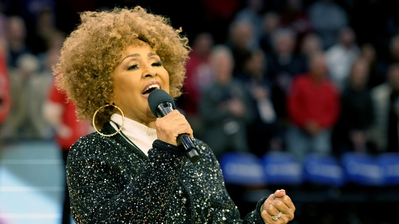 Darlene Love performing the national anthem into microphone at basketball game