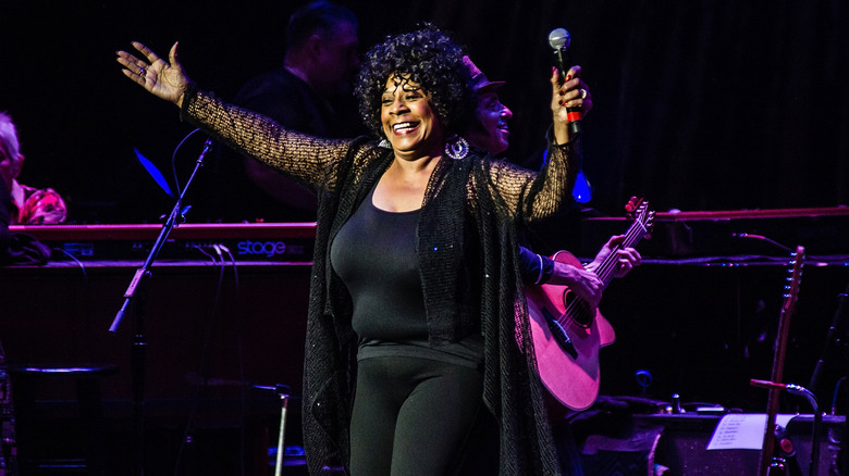 Merry Clayton celebrating on stage with arms open while holding a microphone