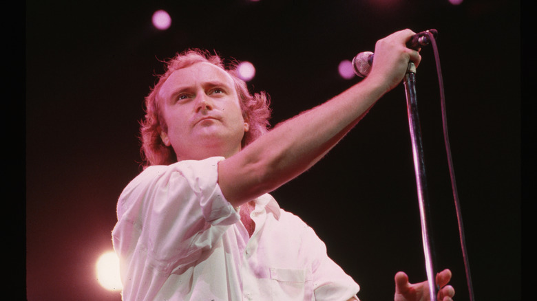 Phil Collins holding microphone on stand in concert