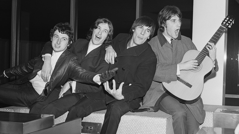 The Kinks sat together laughing and posing with a guitar