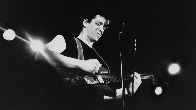Lou Reed playing guitar on stage with dark background