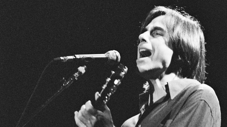 Confessional singer-songwriter Jackson Browne singing and playing guitar in front of microphone