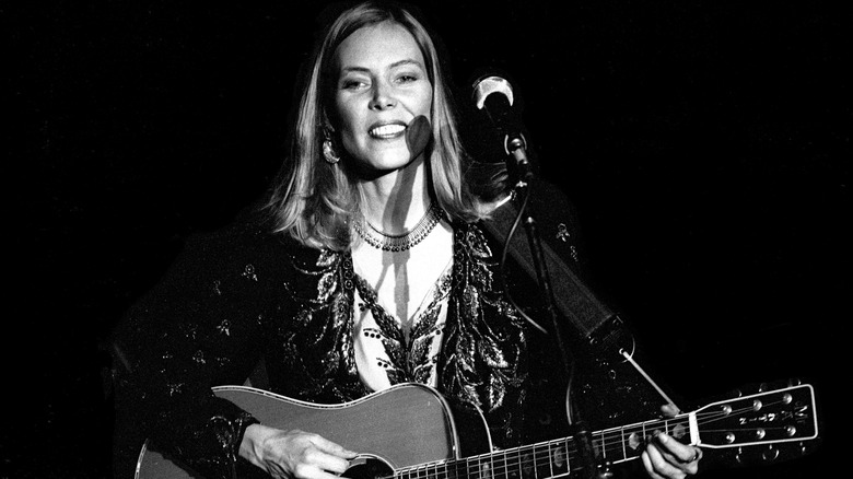 Joni Mitchell smiling with guitar on stage