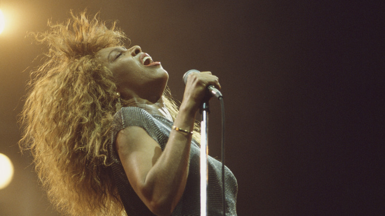 Tina Turner performing with head thrown back while holding the microphone