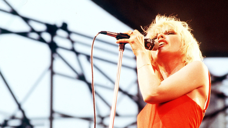 Debbie Harry onstage with microphone in orange dress