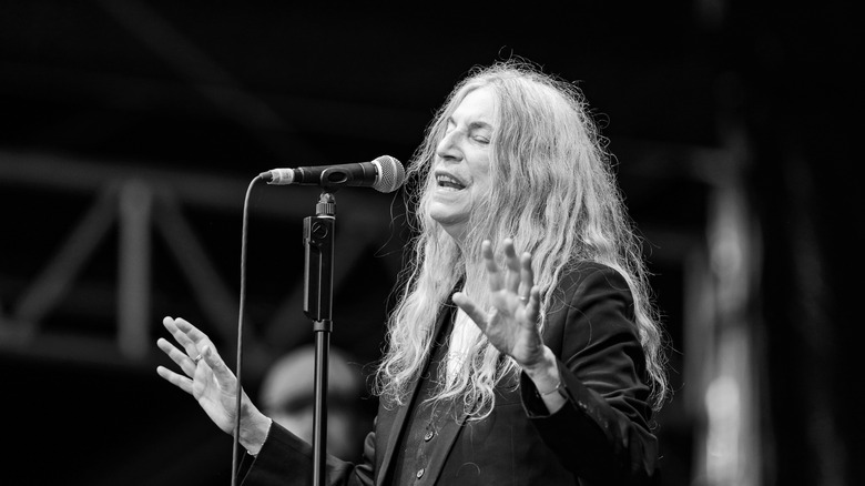Patti Smith singing in front of microphone with arms out and eyes closed