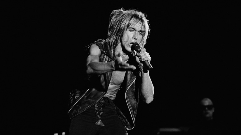Iggy Pop of the Stooges singing into mic and extending a hand