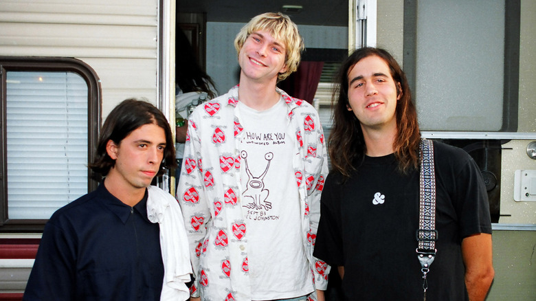 Dave Grohl, Kurt Cobain, and Krist Novoselic posing outside a trailer