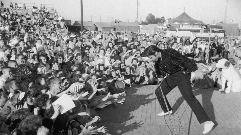 Elvis Presley performing in daytime with adoring audience reaching toward him