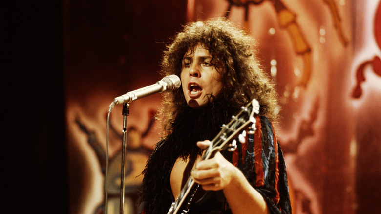 Mark Bolan in glam rock outfit singing and playing guitar on stage