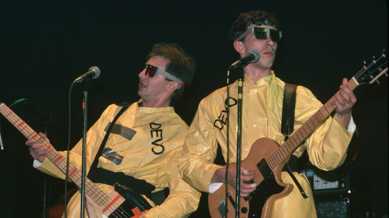 two members of Devo performing onstage in yellow jumpsuits and sunglasses