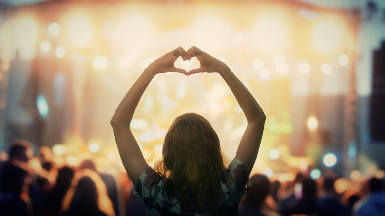 woman making heart shape with hands at a concert