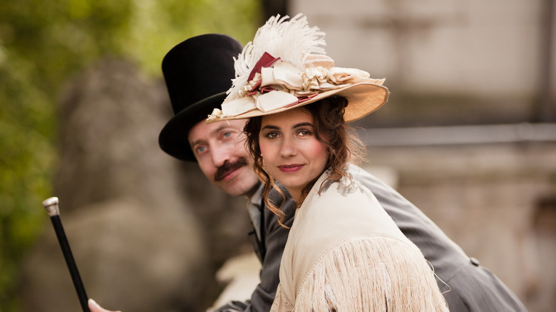 Hatted Victorian couple leaning against banister