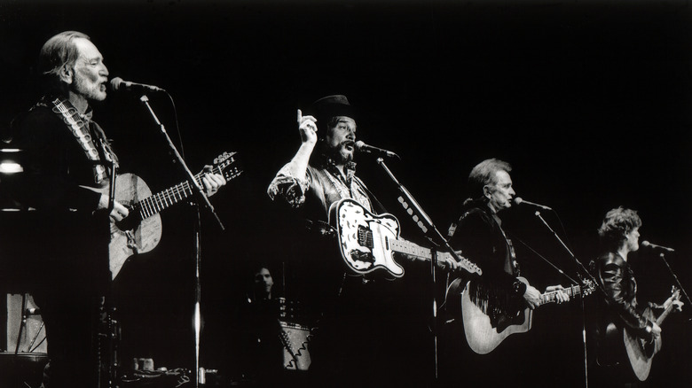 Willie Nelson, Waylon Jennings, Johnny Cash, and Kris Kristofferson on stage singing and playing guitars
