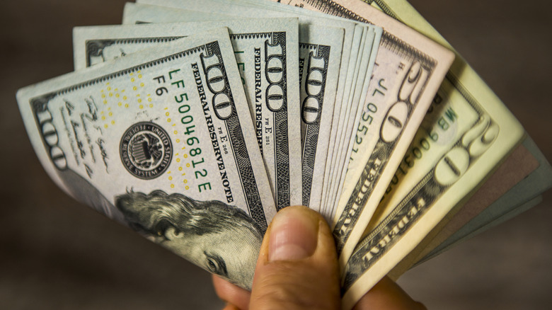 A hand holding folded U.S. dollar bills.