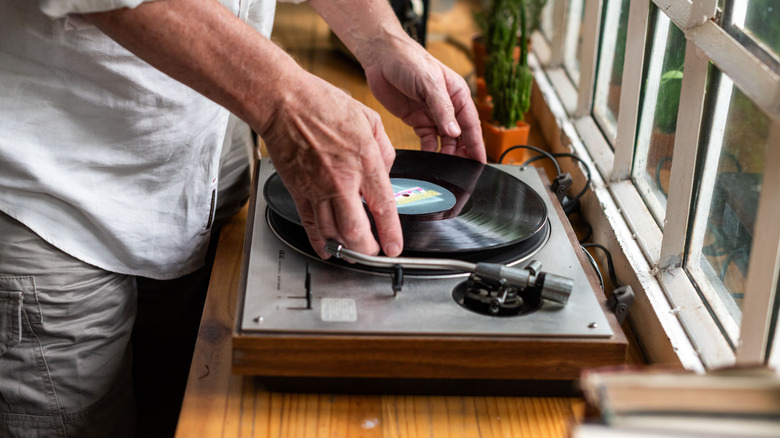 A man placing a vinyl record on a turntable by the window.