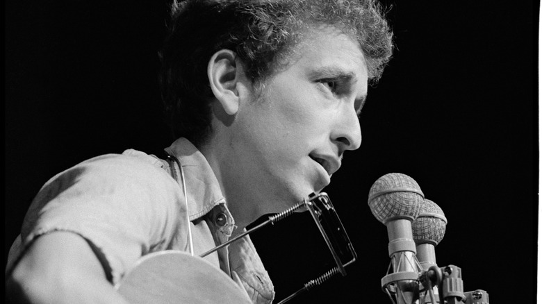 Bob Dylan singing at mic wearing harmonica neck rack