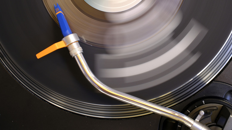 A chrome tonearm with a blue cartridge and an orange anti-skate device