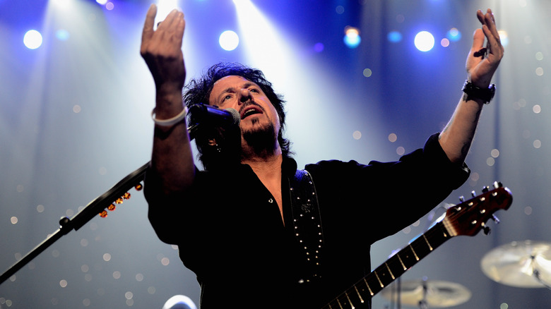 Steve Lukather of Toto singing with arms raised on stage