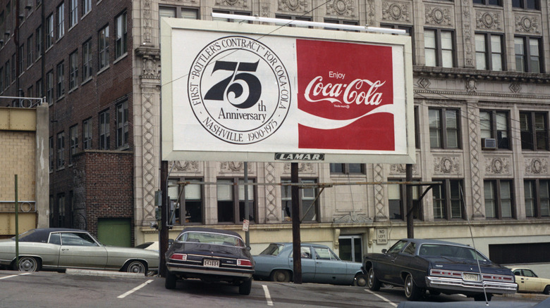 Coca-Cola billboard in '70s parking lot by buildings