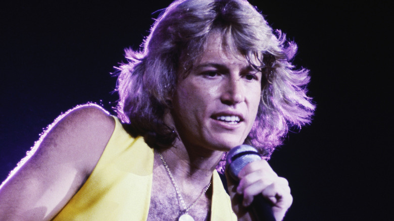 Andy Gibb in yellow vest and medallion singing on stage