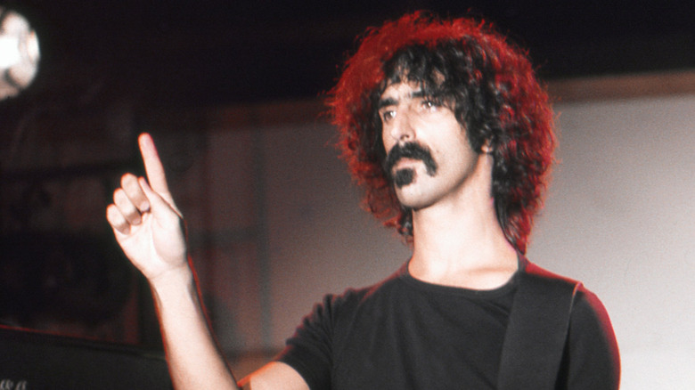 Frank Zappa standing in spotlight with guitar