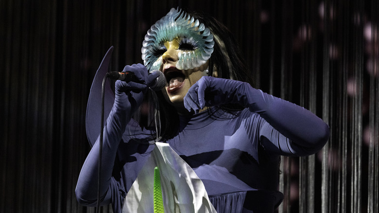 Bjork wearing a blue bodysuit with appendages and a face mask while performing