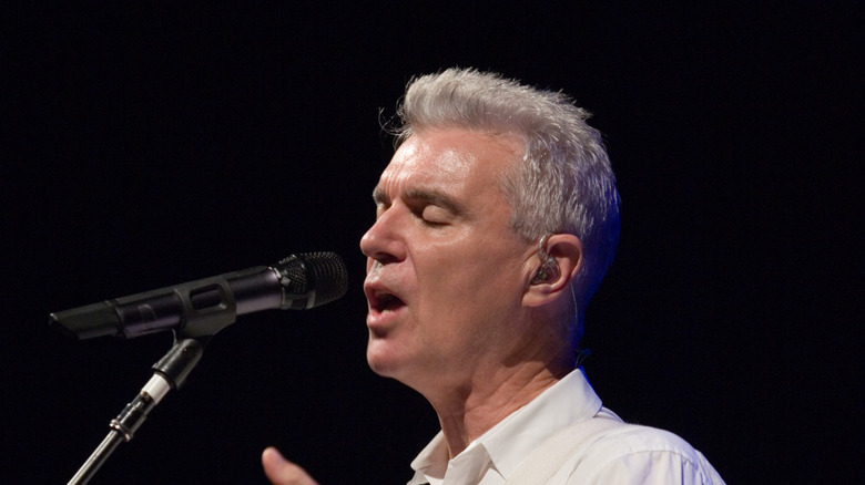 David Byrne singing into a microphone onstage