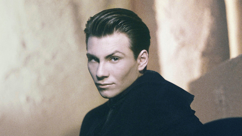 Christian Slater smirking with slicked back hair in black jacket