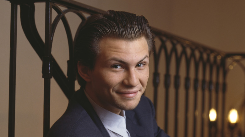 Christian Slater smiling in suit by railing indoors