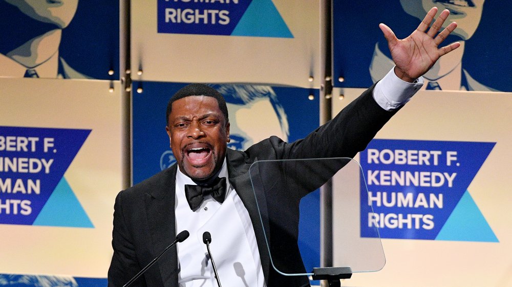 Chris Tucker speaking at event in tux arm raised