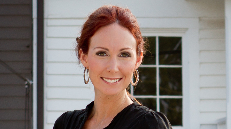 Shannon Richardson smiling with hoop earrings in front of white house