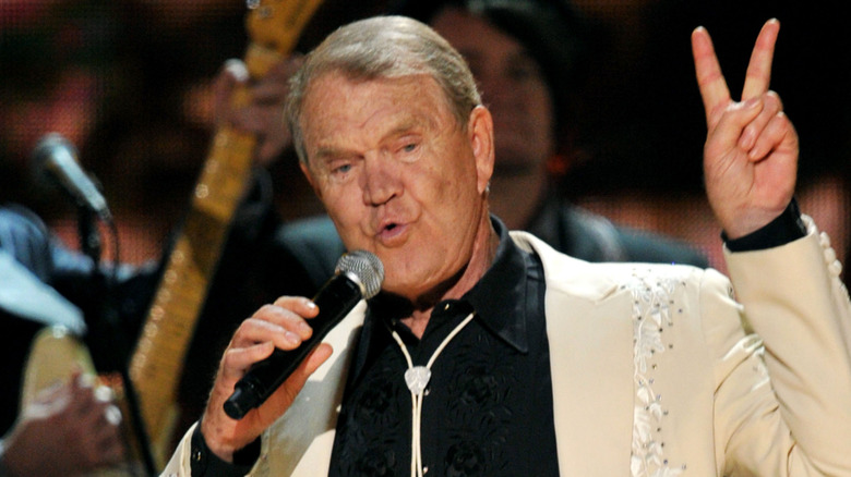 Glen Campbell singing with hand up showing V fingers