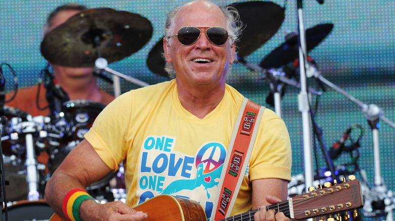 Jimmy Buffett smiling wearing sunglasses playing guitar on stage